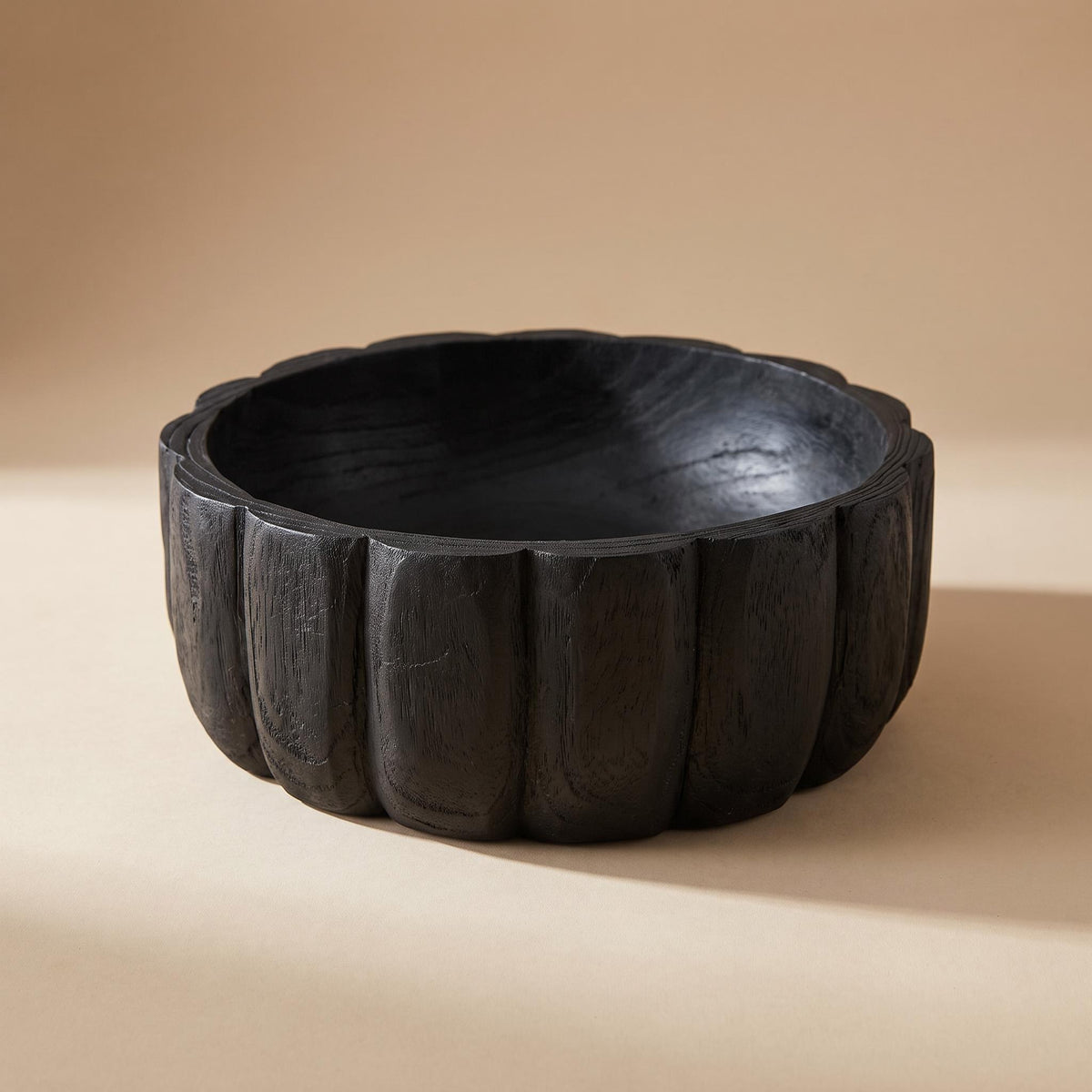 Ondel carved black wooden bowl with vertical lobes, empty, on a warm neutral background