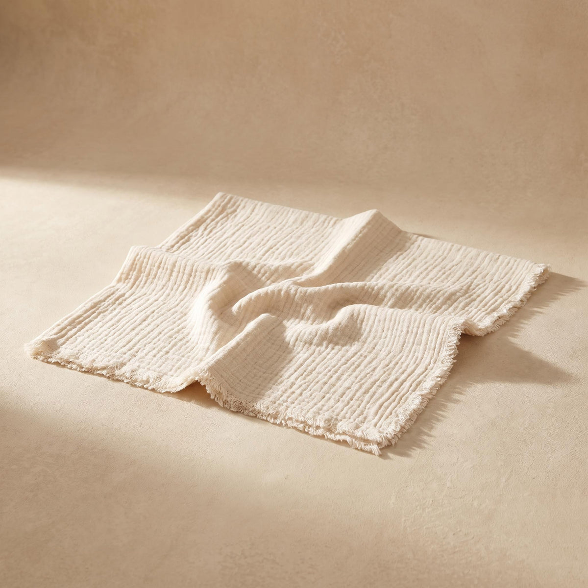 Gasa undyed double-gauze cotton napkin with a raw frayed edge, on a warm neutral background