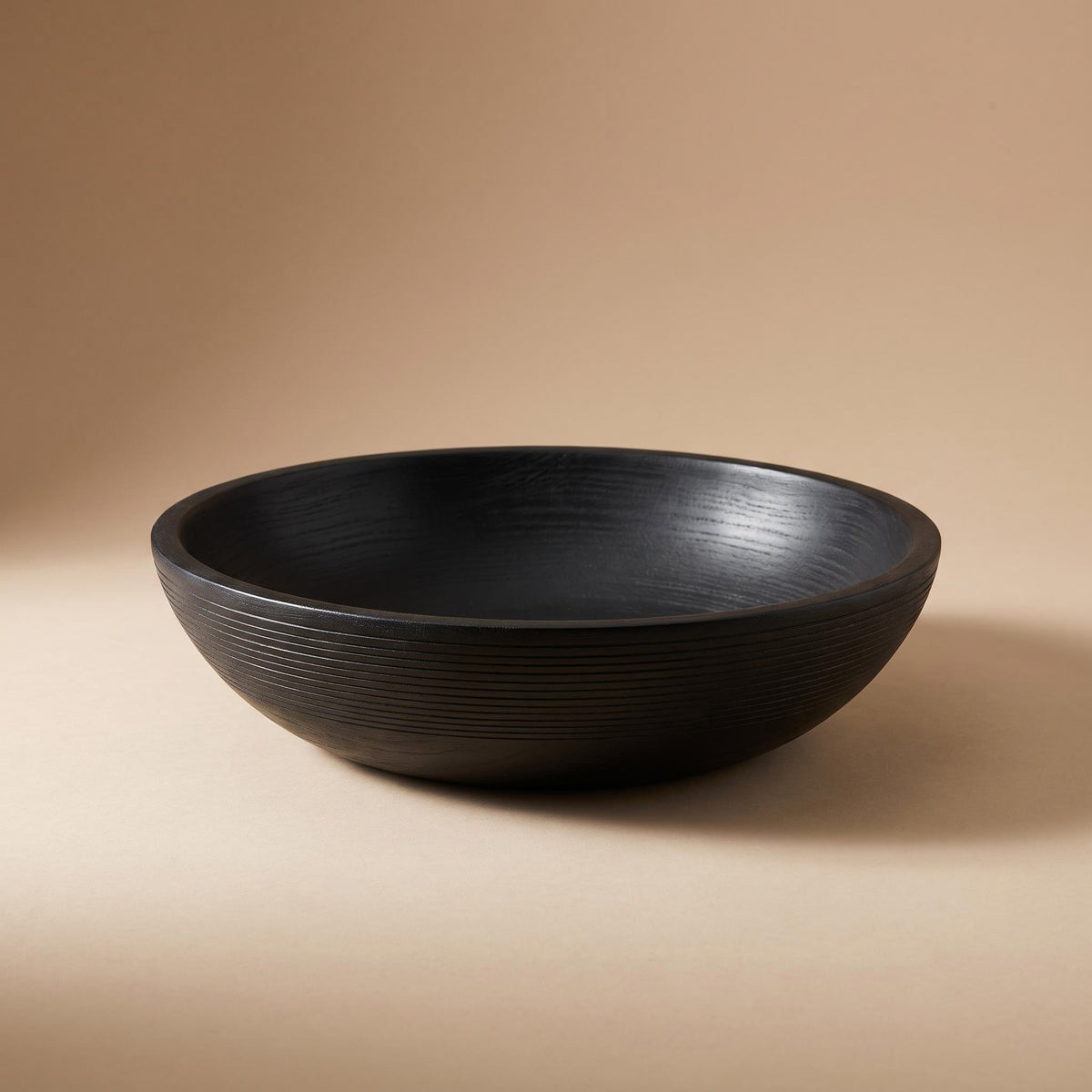 Korren ribbed matte black wooden bowl, empty, on a warm neutral background