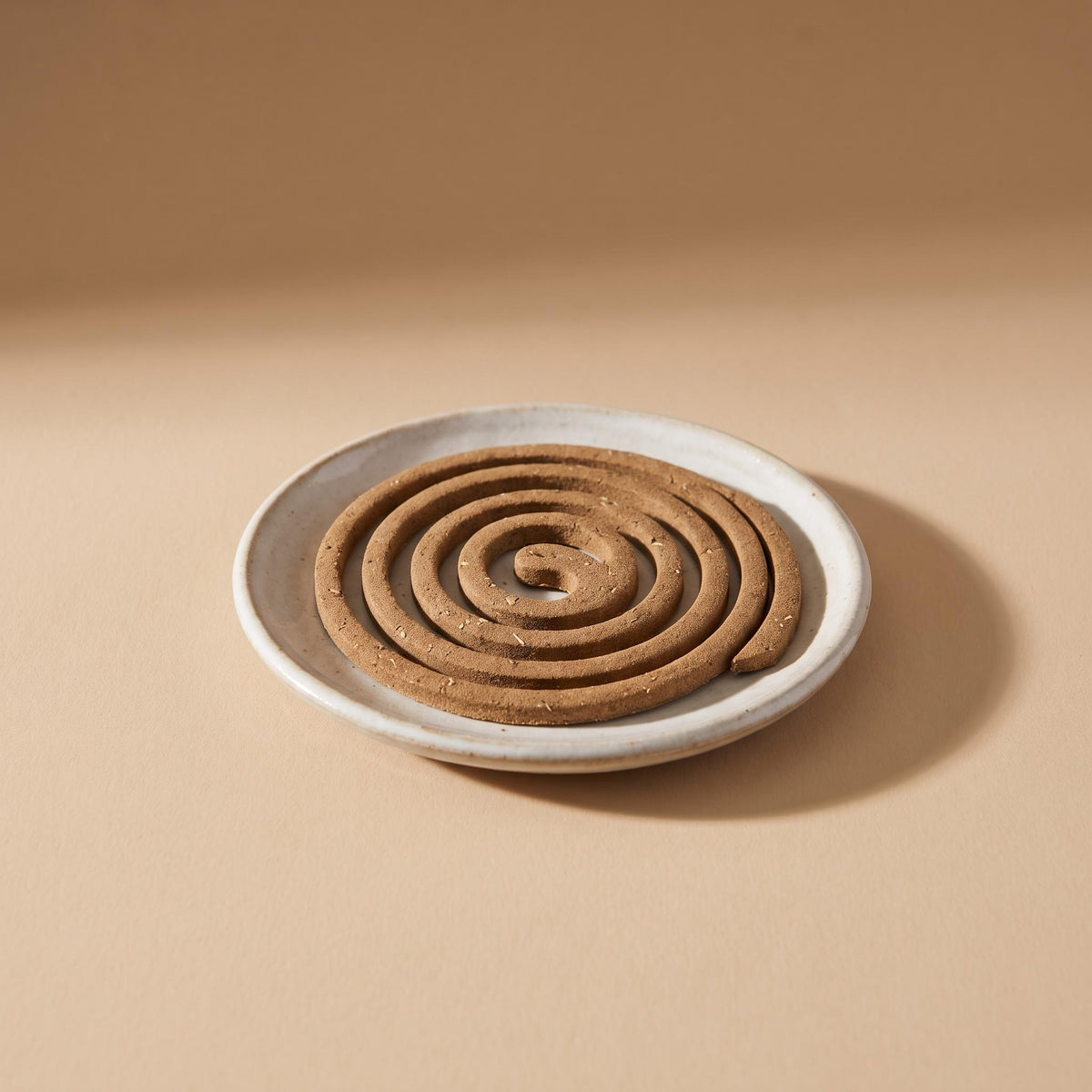 Espiral flat incense coil on a shallow ceramic dish, on a warm neutral background