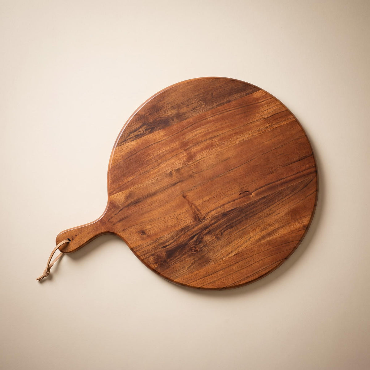 Albo round acacia serving board with leather cord, empty, on a warm neutral background