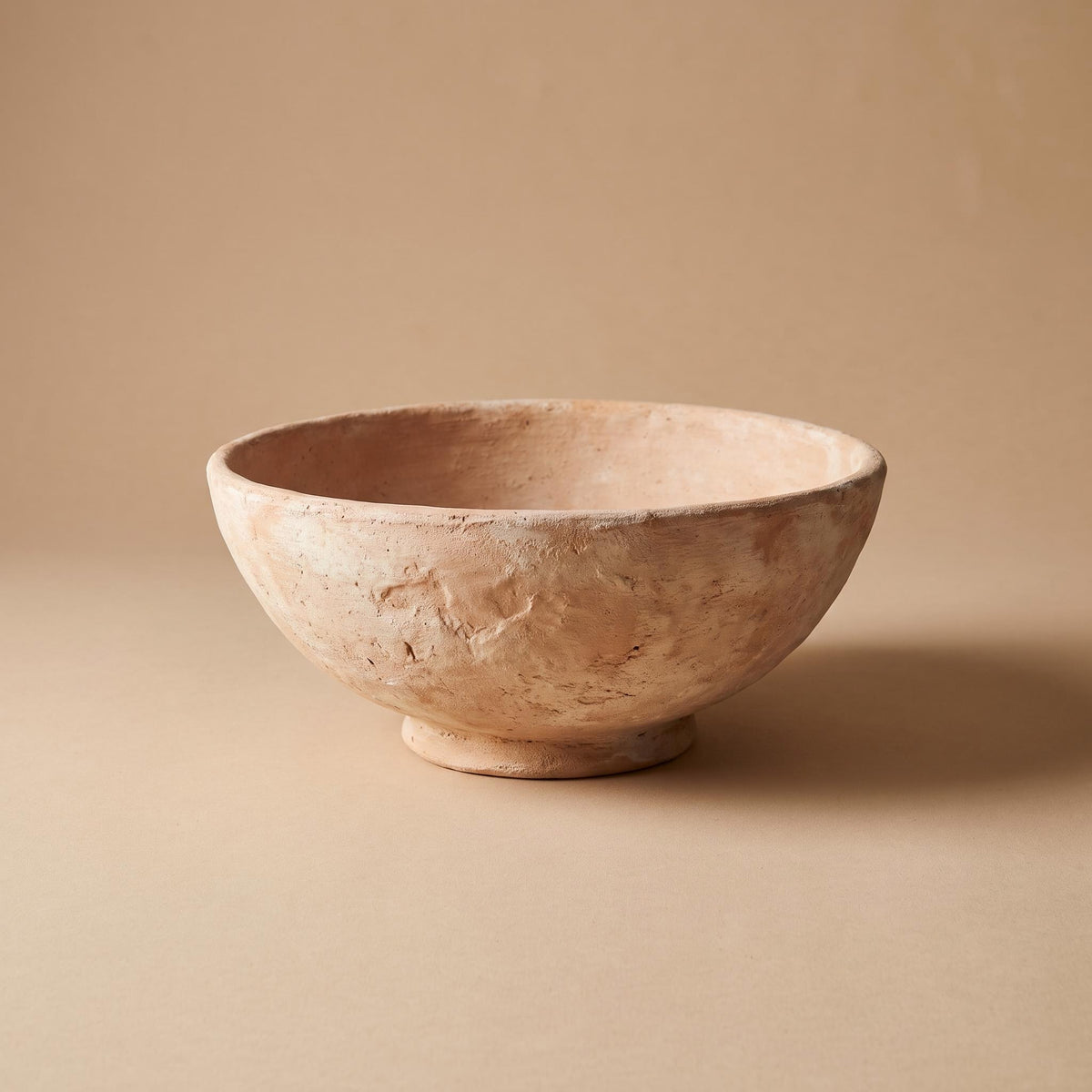 Cálida unglazed clay bowl on a low foot, empty, on a warm neutral background