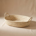 Marea shallow oval seagrass basket with a handle at each end, empty, on a warm neutral background