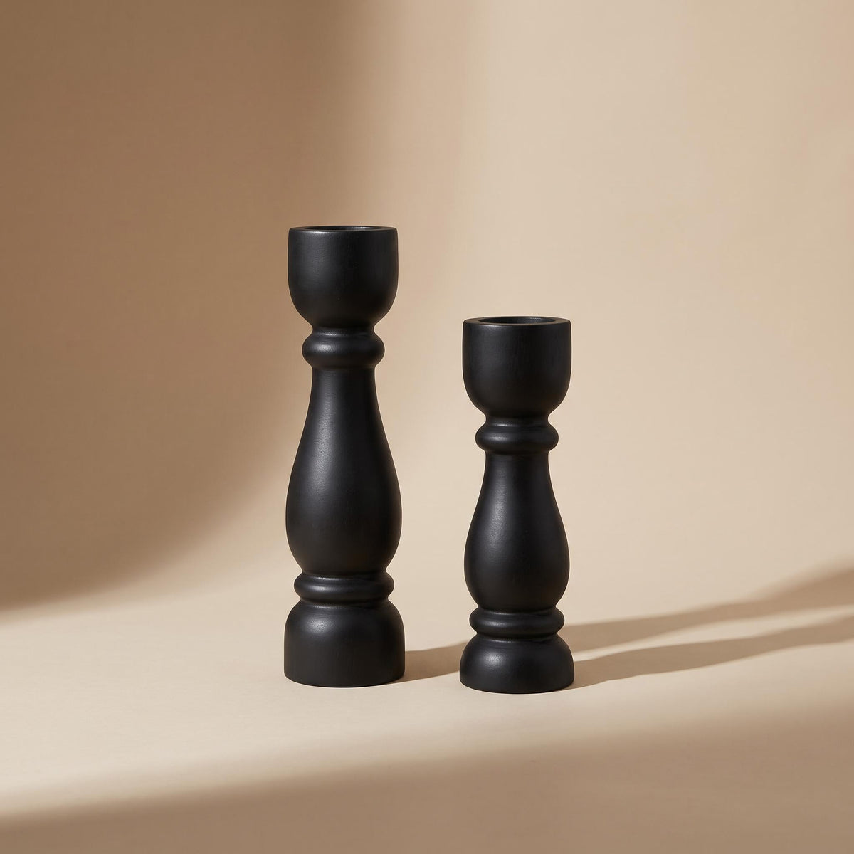 Pilvo pair of turned matte black wooden candle holders, unlit, on a warm neutral background