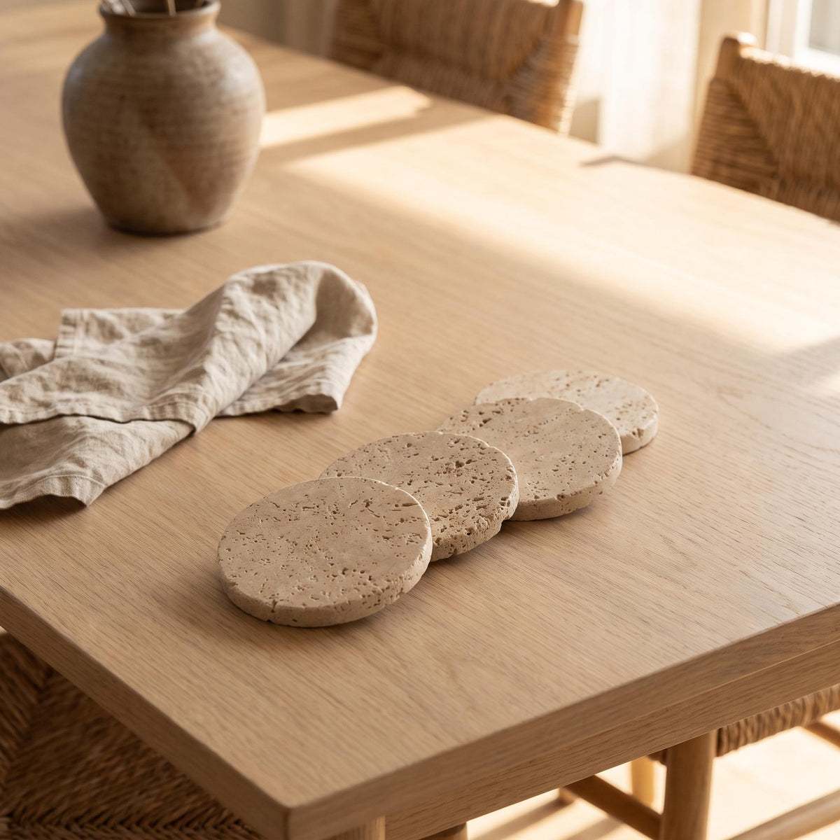 Four Pietra coasters laid out on a dining table beside a linen napkin