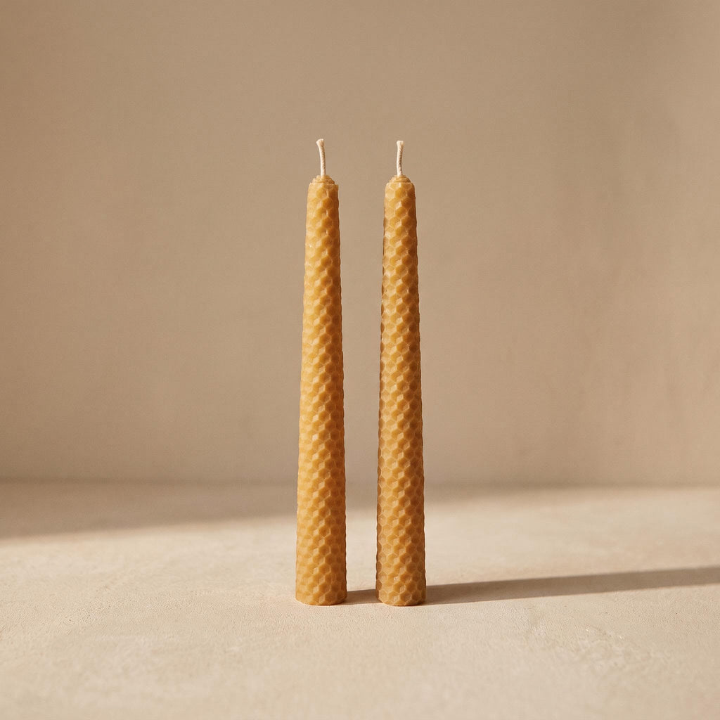 Panal pair of rolled beeswax candles with honeycomb texture, unlit, on a warm neutral background
