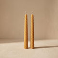 Panal pair of rolled beeswax candles with honeycomb texture, unlit, on a warm neutral background