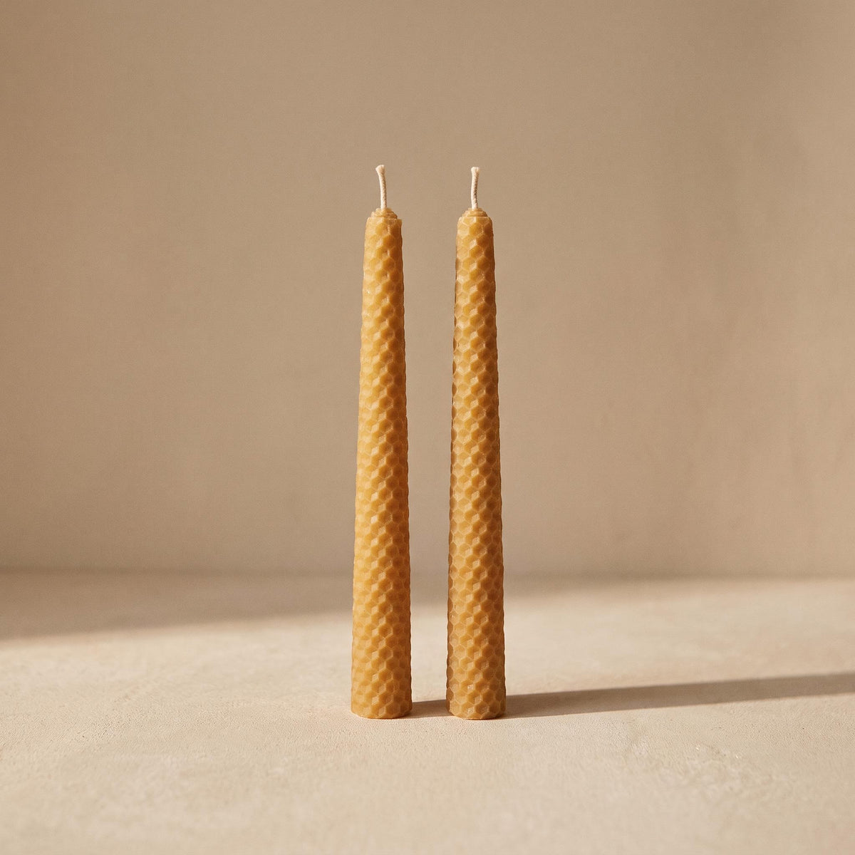 Panal pair of rolled beeswax candles with honeycomb texture, unlit, on a warm neutral background