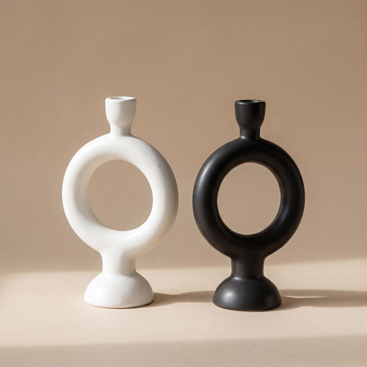 Anel pair of ring candle holders, one white and one black, unlit, on a warm neutral background