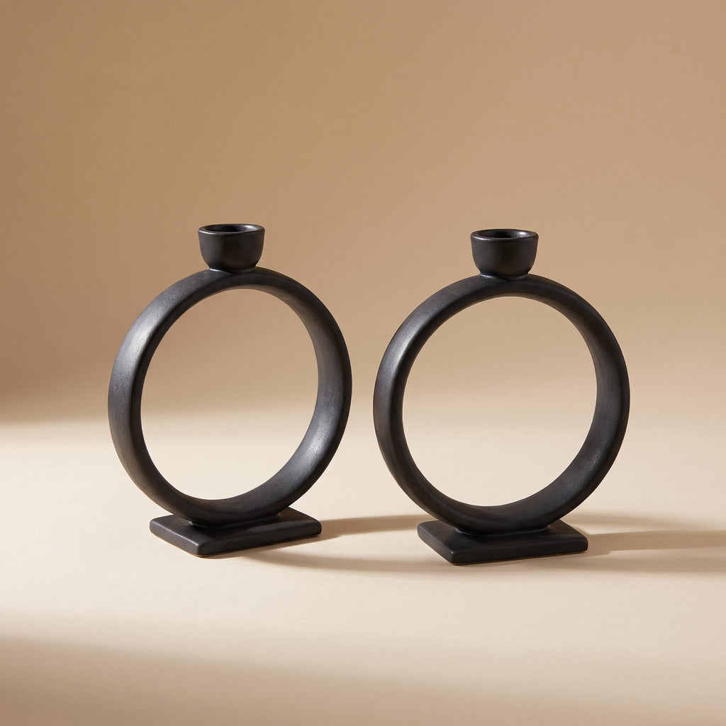 Anel pair of matte black ceramic ring candle holders, unlit, on a warm neutral background