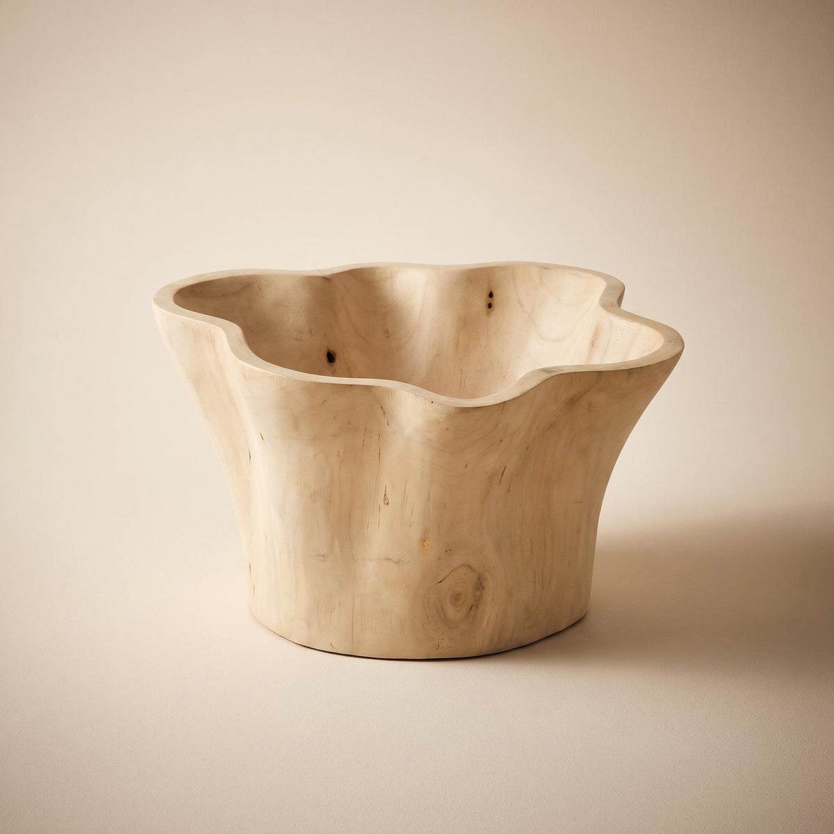 Aurebo carved wooden bowl with an irregular rim that rises and falls, empty, on a warm neutral background