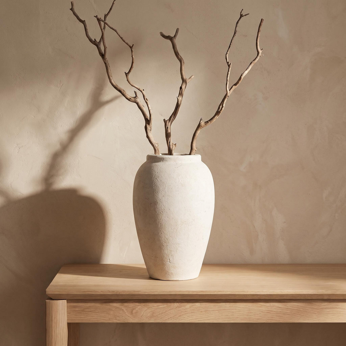 Bianca chalky off-white stoneware urn on a console holding bare dried branches