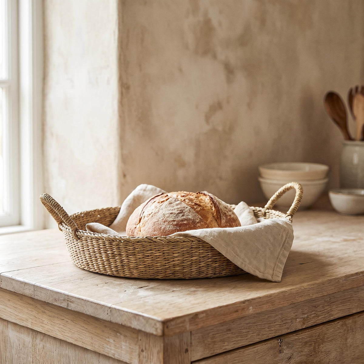 Marea basket on a kitchen counter holding a loaf of bread on a linen cloth